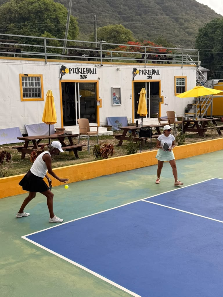 Player at the non-volley zone with the Pickleball268 Antigua clubhouse behind her