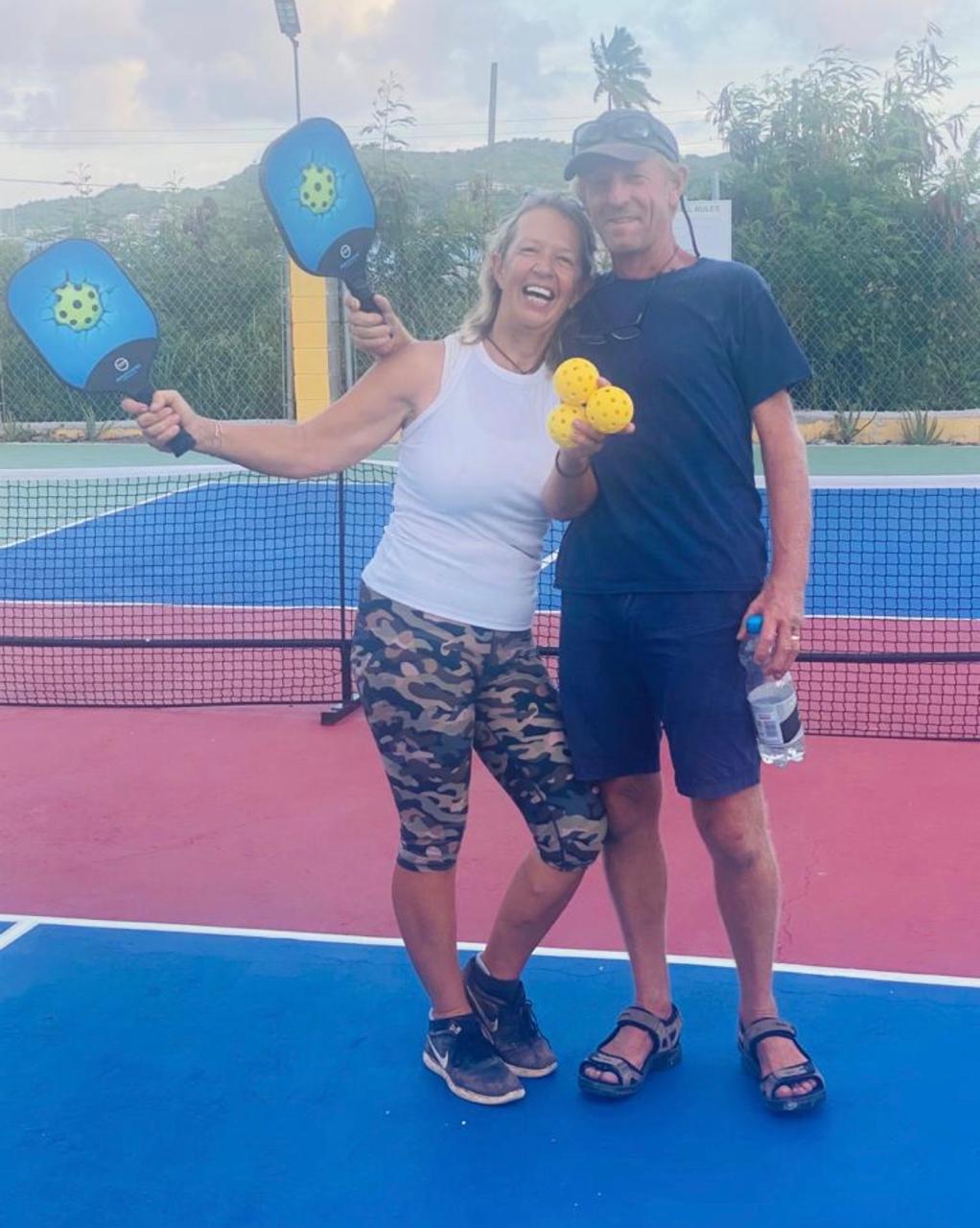 Woman laughing while holding three pickleballs next to a man holding a water bottle