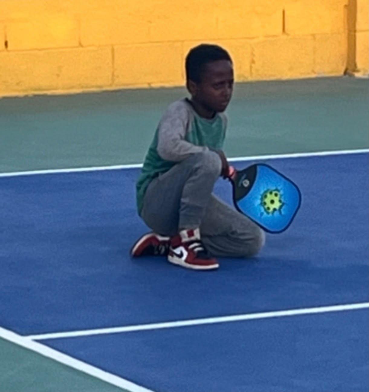 Boy crouching on court holding his paddle, focused