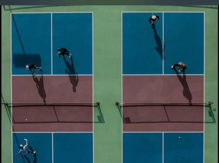 Drone shot looking straight down at two courts with players casting long shadows