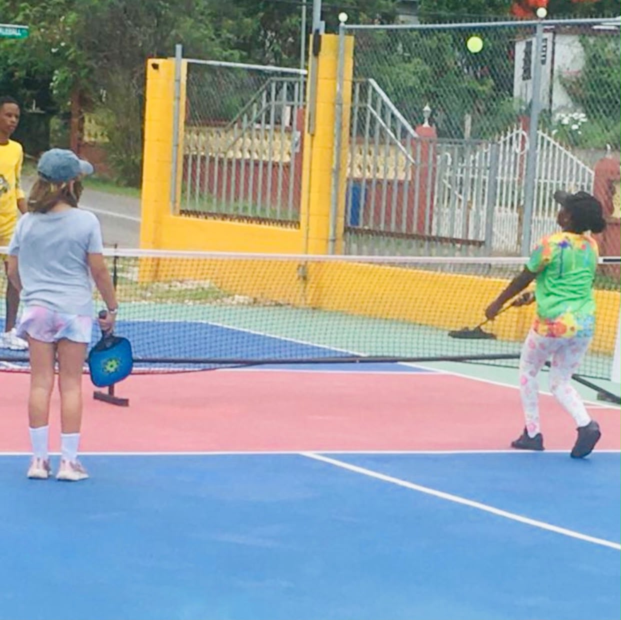 Two young players rallying near the entrance gate of the courts