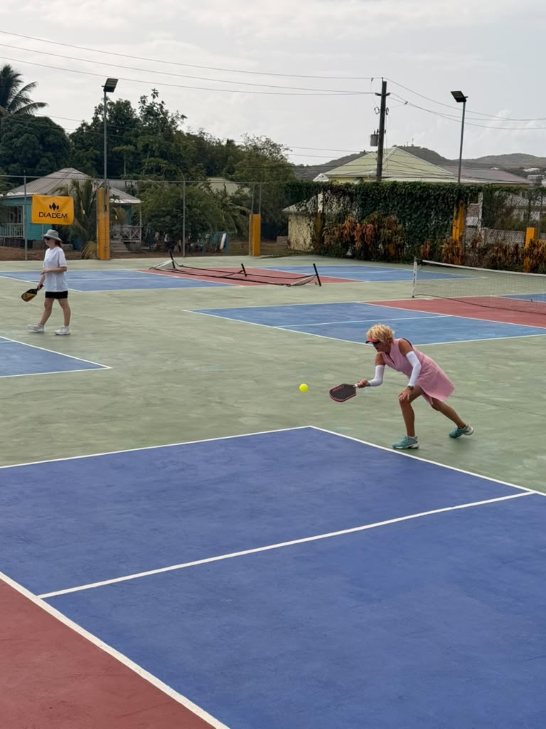 Player in a pink dress hitting a dink shot on the multi-court complex, DIADEM banner in the background