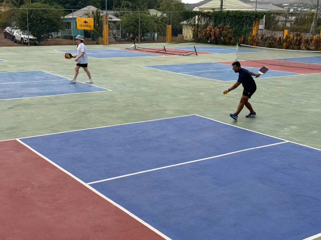Two players walking across the courts between points, DIADEM banner and parked cars behind them