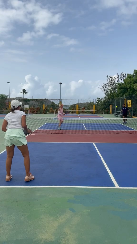 Players rallying on court with the sea and hills visible in the background