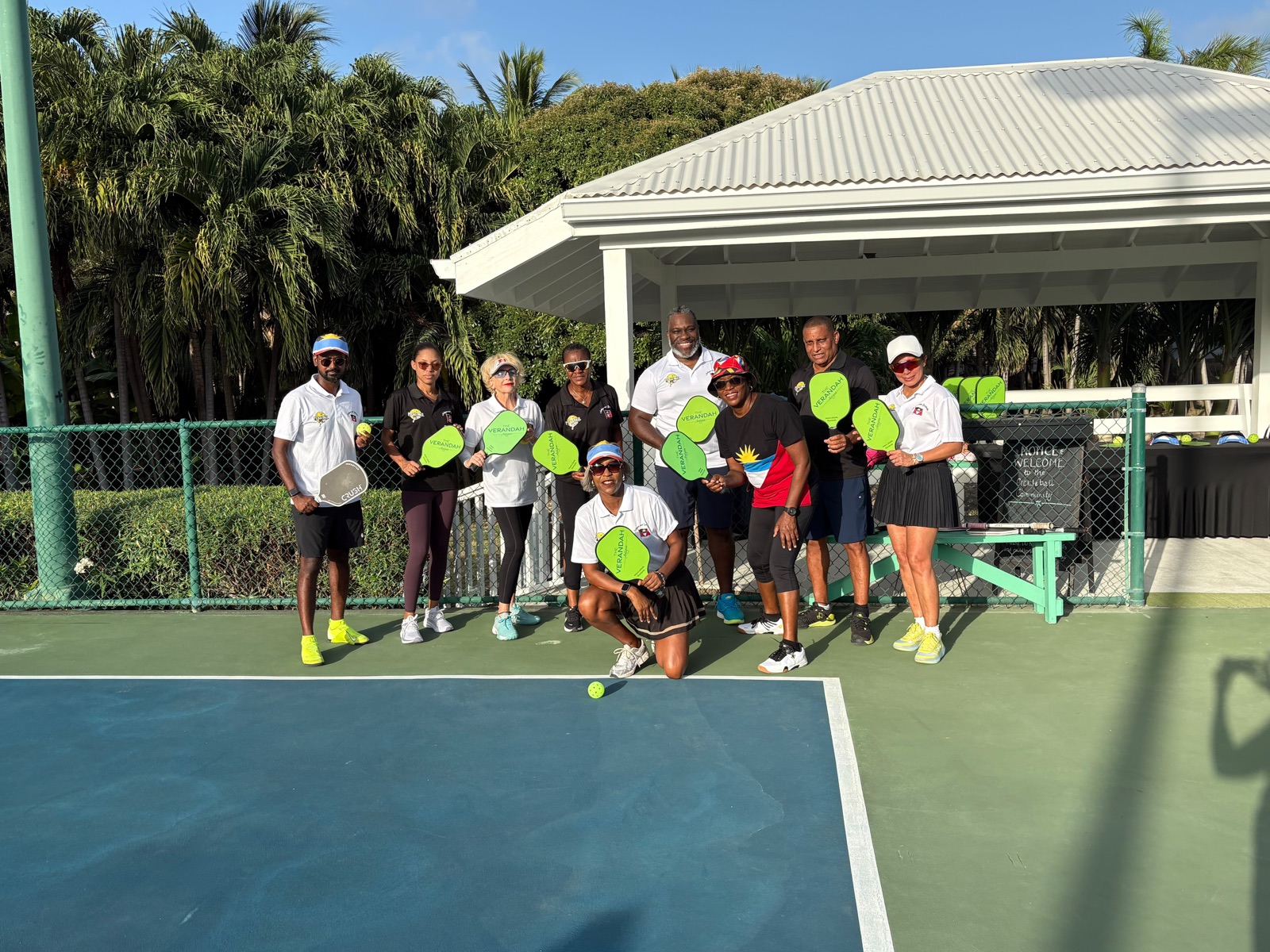 Group posing with green paddles under a pavilion at The Verandah resort courts